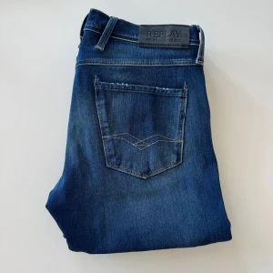 Replay Anbass jeans blå, stl 30/30 - Snygga blå Replay Anbass jeans i klassisk femficksmodell. Jeansen har en smal passform med raka ben, diskreta slitningar och snygga detaljer på bakfickorna. Tillverkade i stretchig denim för extra komfort. Perfekta för dig som gillar stilrena och moderna jeans.