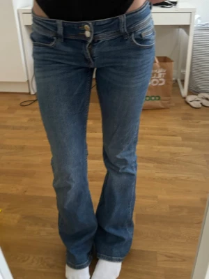 Blå bootcut jeans med låg midja - Säljer ett par blå bootcut jeans med låg midja och dubbla knappar framtill. Midjemått: 35cm, innerbenslängd: 78cm, storlek 158 från barn Gina