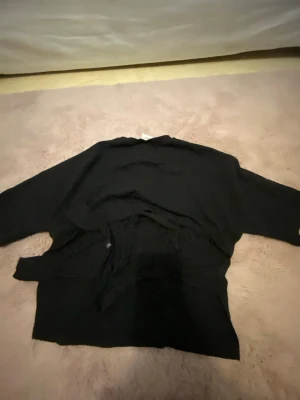 svart t shirt öppen rygg knyter - Svart stickad cardigan med lång ärm och knytband i midjan. Enkel och stilren design, perfekt att slänga över en t-shirt eller topp. Mjuk och skön känsla tack vare det stickade materialet.