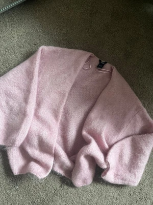 Ljusrosa kofta från Lindex - Mysig ljusrosa kofta från Lindex i stickad, fluffig kvalitet. Koftan har öppen front och långa ärmar, perfekt för lager-på-lager och en chill look. Passar dig som gillar en söt och enkel stil.