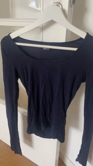 Mörkblå långärmad topp Gina Tricot - En enkel och stilren mörkblå långärmad topp från Gina Tricot. Modellen har en bred, rund ringning och är gjord i mjukt bomullsmaterial. Perfekt att matcha med jeans eller kjol för en clean look.