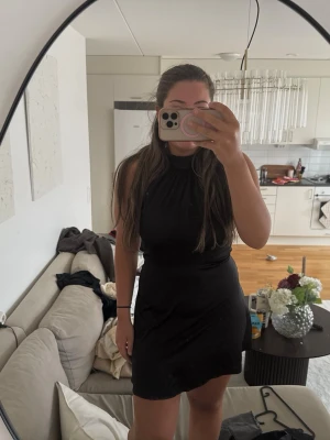 Svart ärmlös kortklänning - Snygg svart kortklänning med hög hals och ärmlös design. Klänningen har en enkel och stilren look med lätt utställd kjol och mjukt, följsamt material. Perfekt för dig som gillar minimalistisk stil och vill ha något som känns både bekvämt och trendigt.