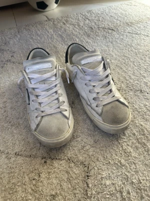 Philippe Model vita sneakers - Snygga vita sneakers från Philippe Model med svarta detaljer på hälen och den klassiska sköldloggan på sidan. Skorna har vita skosnören och en låg siluett. Tillverkade i läder med mockadetaljer för en trendig look. Tyvärr är boxen sönder 