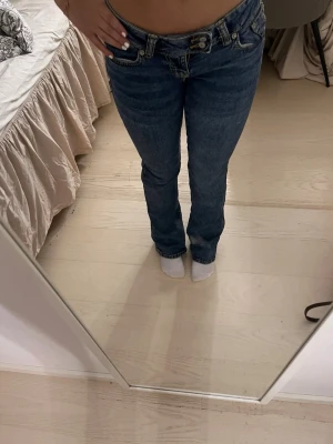Mörkblå bootcut jeans med låg midja - Säljer ett par mörkblå bootcut jeans med låg midja och dubbla knappar i linningen. Jeansen har klassisk femficksdesign och är tillverkade i denim. Perfekta för dig som gillar en retro vibe och vill ha en snygg siluett. Short xxs