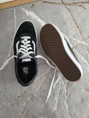 Svarta Vans Old school sneakers - Klassiska Vans Old Skool sneakers i svart mocka och canvas med vit sula och vit sidostripes. Skorna har vita skosnören och den ikoniska gummisulan med rutmönster. Perfekta för en streetwear-look och passar till det mesta.