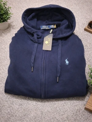 mörkblå hoodie från Polo Ralph  - Snygg mörkblå hoodie från Polo Ralph Lauren med dragkedja och huva med snörning. Den är I storlek M kan även passa S. Tillverkad i 100% mjuk bomull. Vid snabbaffär kan priset diskuteras och även frakta vid det första tillfället.