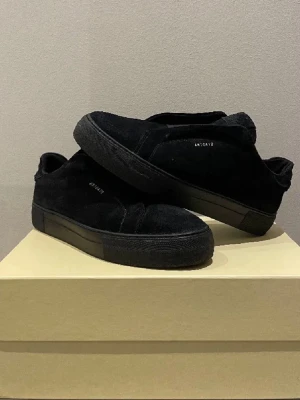 Svarta sneakers från Axel Arigato - Stilrena svarta sneakers från Axel Arigato i mocka med diskret logga på sidan. Skorna har en chunky svart sula och minimalistisk design utan synliga snören. Perfekta för dig som gillar en clean och modern look.