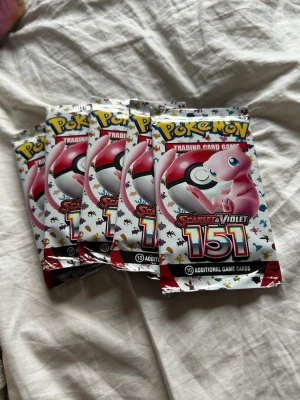 Pokémon Scarlet & Violet 151 boosterpack - Säljer flera Pokémon Scarlet & Violet 151 boosterpack med 10 samlarkort i varje. Förpackningarna är färgglada med motiv av Mew och Pokéboll, perfekt för dig som samlar eller spelar Pokémonkort. 5 packs oöppnade