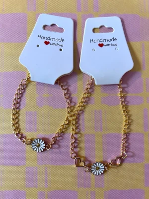 Mor- och dotter armband med prästkrage - Två handgjorda armband i guldfärgad metall med kedja, dekorerade med en vit och gul prästkrage samt små hjärtan.  Lätta att matcha med andra smycken och passar extra bra som mor- och dotter armband.