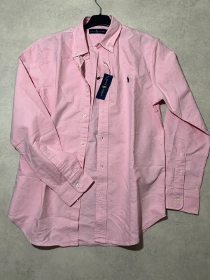 Ralph Lauren - Två skjortor från Ralph Lauren i en snygg rosa färg med ikonisk broderad logga på bröstet. Perfekt för en clean och fräsch look funkar både till vardag och uppklätt.