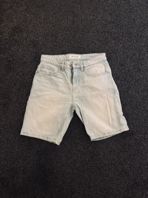 Ljusblå jeansshorts - Säljer ett par ljusblå jeansshorts från Weekday med klassisk femficksdesign och knappgylf. Shortsen har normal passform och är tillverkade i bomull, perfekta för en chill sommarlook.
