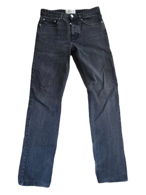 Svarta raka jeans från Ami - Snygga svarta jeans från Ami Paris med rak passform och klassisk femficksdesign. Jeansen har silverfärgade knappar och är tillverkade i ett robust denimtyg. Perfekta för en stilren och avslappnad look. Skick: 9/10. Digitalt kvitto finns.