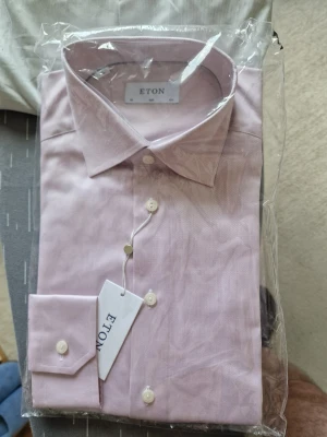 Ljusrosa skjorta från Eton slim fit - Snygg ljusrosa skjorta från Eton i slim fit-modell. Skjortan har klassisk krage, långa ärmar och knappar framtill. Tillverkad i bomull och passar perfekt till en stilren look. Märkeslapp och etikett kvar.