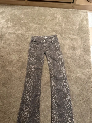 Grå leopardmönstrade bootcut jeans - Säljer ett par jeans med leopardmönster och bootcut-modell. klassiska fickor fram och bak samt knapp- och dragkedjestängning. Perfekta för dig som vill sticka ut med ett djurmönster i din outfit.