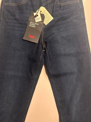 Levi's Mile High Super Skinny jeans 25*28 - Mörkblå jeans från Levi's i modellen Mile High Super Skinny. Jeansen har hög midja, supertight passform och klassiska gula sömmar. Tillverkade i stretchigt denim för extra komfort. Perfekta för dig som gillar en slimmad siluett och modern look.