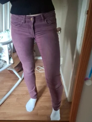 Lila skinny jeans med hög midja - Säljer ett par lila skinny jeans med lågmidja och klassisk femficksdesign. Jeansen har smal passform och stängs med knapp och dragkedja. Perfekta för dig som gillar färg och vill sticka ut lite extra.