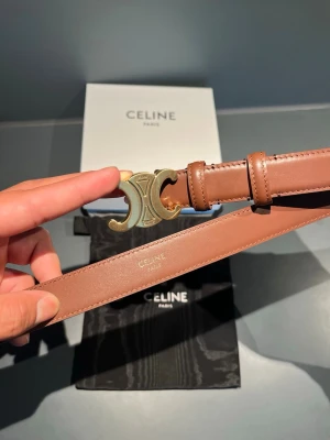 Brunt bälte från Celine med gulddetalj 95 cm - Snyggt brunt bälte från Celine med ikoniskt guldspänne i form av deras Triomphe-logo. Skärpet är gjort i slätt skinn och har stilrena sömmar. Perfekt accessoar för att lyfta din outfit med en lyxig touch. 