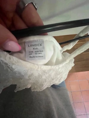 Skolavslutningsklänning - Superfin vit klänning från Lindex med spetsdetaljer och oneshoulder-design. Klänningen har en kort längd och är perfekt för somriga dagar eller speciella tillfällen. Den har en markerad midja och är tillverkad i ett lätt material.
