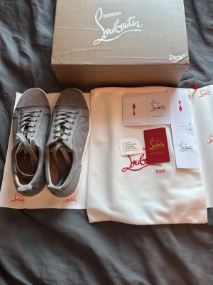 Gråa sneakers från Christian Louboutin - Snygga gråa sneakers från Christian Louboutin i mocka med klassisk låg siluett. Skorna har matchande grå snörning och diskreta detaljer. Kommer med originalkartong, dustbag och äkthetskort. Perfekta för dig som vill ha en exklusiv och stilren look.