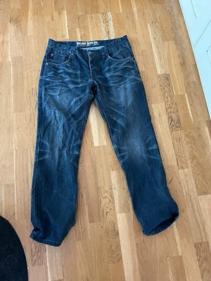 Mörkblå raka jeans - Säljer ett par mörkblå jeans med raka ben och klassisk femficksdesign. Jeansen har ljusa slitningar och kontrastsömmar, vilket ger en avslappnad och trendig look. Perfekta för dig som gillar en enkel och stilren stil.