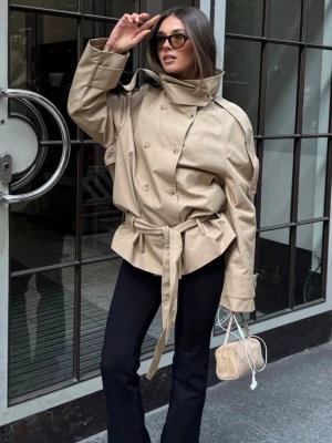 Beige trenchcoat  - Trendig och SLUTSÅLD (helt ny med lappar kvar)  beige trenchcoat med dubbelknäppning, breda slag och hög krage. Jackan har ett matchande knytbälte i midjan och vida ärmar för en cool siluett. Perfekt för dig som vill ha en modern och stilren look.