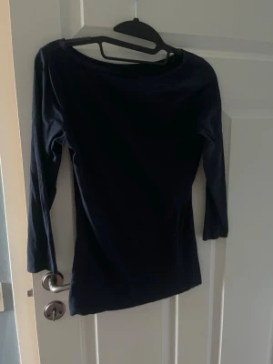 Mörkblå långärmad topp - En stilren mörkblå topp med lång ärm och rund halsringning. Toppen har en figurnära passform och är tillverkad i ett mjukt material som känns bekvämt mot huden. Perfekt att matcha med jeans eller kjol för en enkel och snygg look.