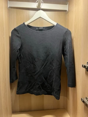 Svart topp med trekvartsärm från Vanilja - En stilren svart topp från Vanilja med rund halsringning och trekvartsärm. Toppen har en lätt ribbad struktur och är i ett mjukt material som sitter snyggt på kroppen. Perfekt att matcha med både jeans och kjol. Aldrig använd