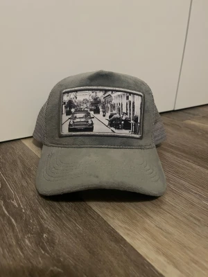 Grå emilio pendenza keps med tryck - Snygg grå truckerkeps med böjd skärm och mesh på sidorna, samt frotté som material. Framtill finns ett svartvitt fototryck av en gata med bilar och byggnader. Perfekt accessoar för en avslappnad streetstyle-look. Pris kan absolut diskuteras.