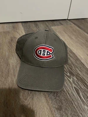 Grå Montreal Canadiens keps - Säljer en grå keps med Montreal Canadiens logga broderad framtill. Klassisk böjd skärm och justerbar baksida. Tillverkad i bomullstyg och perfekt för dig som vill representera ditt favoritlag med stil. Pris kan absolut diskuteras.