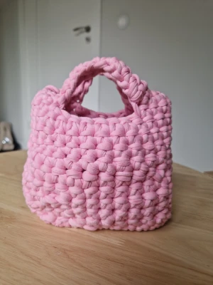  virkad handväska med handtag - Superfin handväska virkad i tröjgarn , helt i ljusrosa. Väskan har en mjuk och fluffig känsla med korta handtag och en boxig form. 