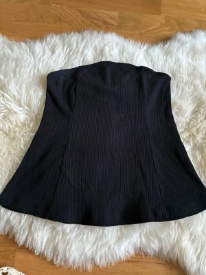Svart ribbad korsett Bik Bok - Säljer en svart korsett från Bik Bok i storlek S. Toppen är ribbad och axelbandslös med en snygg, figurnära passform. Perfekt för att skapa en cool och trendig look. Materialet är mjukt och stretchigt för extra komfort.
