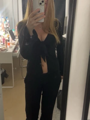 Svart långärmad topp med knyt - Trendig svart långärmad topp med djup v-ringning och knyt framtill. Toppen är croppad och har en smickrande passform som framhäver midjan. Perfekt för dig som vill ha en stilren men ändå edgy look.