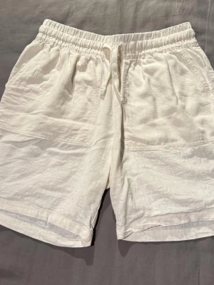 Vita/beiga Pegador linneshorts - Säljer ett par vita shorts i linne med avslappnad passform och elastisk midja med snörning från Pegador. Shortsen har fickor fram och en bakficka, perfekta för varma dagar. Stilrena och lätta att matcha till olika outfits. Storlek XS men är stora i storleken. Se bild 3 för att se hur de sitter på mig (är 178 och väger 75kg). Helt nya och oanvända. 