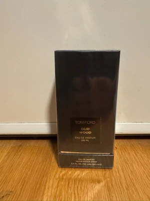 Tom Ford Oud Wood Eau de Parfum 100ml - Tom Ford Oud Wood Eau de Parfum 100ml i elegant mörkgrå förpackning med guldiga detaljer. Lyxig och exklusiv doft med träiga och varma toner. Perfekt för dig som gillar unika och sofistikerade parfymer.