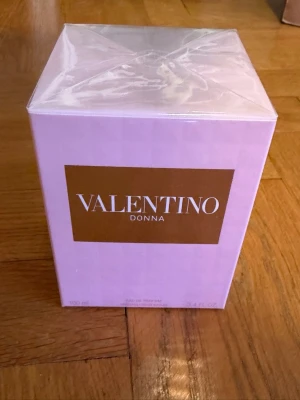 Valentino Donna parfym 100 ml - Säljer en lyxig parfym från Valentino, Donna. Förpackningen är ljusrosa med en elegant guldbrun etikett och är tillverkad av kartong. Perfekt för dig som vill ha en exklusiv doft i snygg design.