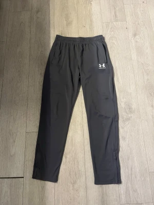 Under Armour byxor  - Snygga svarta träningsbyxor från Under Armour med elastisk midja och två sidofickor. Byxorna har en smal passform och är tillverkade i ett lätt och stretchigt material som passar perfekt för träning eller sportaktiviteter.