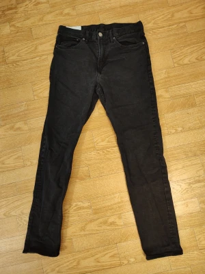 Svarta jeans herr stl 33/34 - Säljer ett par svarta skinny jeans med klassisk femficksdesign och dragkedjegylf. Jeansen har en smal passform och är tillverkade i stretchigt denimtyg för extra komfort. Perfekta för en trendig och avslappnad look.