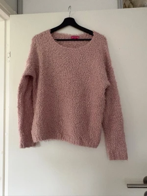 Ljusrosa fluffig stickad tröja - Mysig ljusrosa stickad tröja med fluffig och texturerad yta. Tröjan har rund halsringning och långa ärmar, perfekt för att hålla värmen. Passar dig som gillar en avslappnad och trendig look.