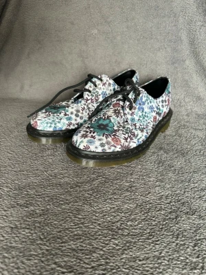 Dr. Martens Floral Shoes – Vintage Style – Leather - 39 - Unika Dr. Martens skor med färgstarkt floralt mönster och klassisk Dr. Martens-sula.  Perfekta om man vill ha ett par Docs som sticker ut lite mer än de klassiska svarta.  Detaljer • Dr. Martens • Floral / blommigt mönster • Klassisk Dr. Martens-sula • Snörning • Stabil och bekväm modell  Passar perfekt till jeans, klänning eller casual outfits.  📦 Skickas snabbt 💬 Hör av dig vid frågor