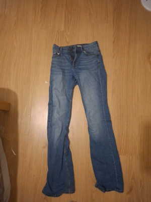 Blå bootcut jeans med låg midja - Säljer ett par klassiska blå bootcut jeans med låg midja och fem fickor. Jeansen har en avslappnad passform och är tillverkade i denim med lätt tvättad look. Perfekta för en casual stil och passar till det mesta i garderoben.