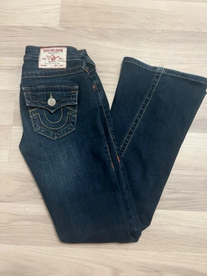 Mörkblå True Religion jeans - Jeans i modellen Joey low rise flare, jättebra skick. Lite slitet längst ner i kanten. Skriv om ni vill ha bild 💗  W- 23, de är uppsydda i butik, vet inte längden men passar mig som är 160 bra