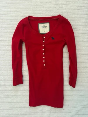 Vintage Abercrombie & fitch Henley med trekvarts ärmar - Sällsynt röd vintage Abercrombie & Fitch 3/4-ärmad Henley-top! Storlek M, passar bättre som S. Mycket gott skick! En rad funktionella knappar som går att öppna eller stänga för att justera stilen. Den klassiska Abercrombie & Fitch älg-loggan i mörkblått broderad på bröstet. Följ för fler liknande kläder och köp gärna bundle/paket!