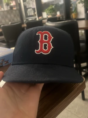 Mörkblå Boston Red Sox keps - Snygg mörkblå keps från New Era med Boston Red Sox-logga broderad i rött och vitt framtill. Klassisk basebollmodell med böjd skärm och ventilationshål. Perfekt för dig som vill ha en sportig och stilren look.
