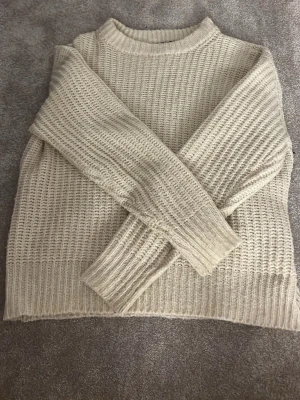 Beige stickad tröja från 157 - Säljer en beige stickad tröja från 157 i storlek S. Tröjan har en rak passform, ribbad halsringning, muddar och nederkant. Materialet är grovstickat och ger en mysig känsla. Tröjan är inte stickig.