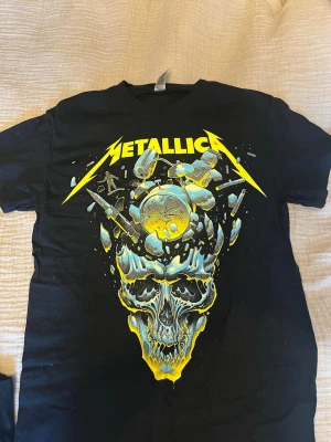Metallica svart band t-shirt - Säljer en svart äkta Metallica t-shirt merch som jag köpt på deras turné. Baksidan har turnélistan för 2023/2024 i gult. Klassisk bandtröja med rund hals och korta ärmar, perfekt för dig som gillar rock och metal.