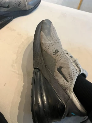 Nike Air Max 270 grå sneakers - Säljer ett par Nike Air Max 270 sneakers i grått med svarta detaljer och blå 270-logga. Skorna har en stor svart luftb soppa i & hälen och meshmaterial på ovandelen för bra ventilation. Klassisk Nike Swoosh på sidan och snörning framtill.