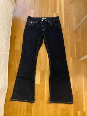 Mörkblå bootcut jeans från Gina Tricot - Storlek 170. Snygga mörkblå bootcut jeans från Gina. Mörkblåa med röda och vita detaljer. Använda ett fåtal gånger. Inga skador och i mycket bra skick.