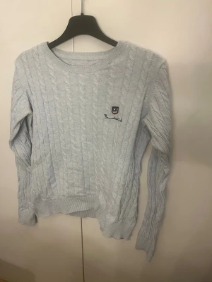 Ljusblå kabelstickad tröja Bondelid - Snygg ljusblå kabelstickad tröja från Bondelid med rund halsringning och ribbade muddar. Tröjan har ett broderat Bondelid-märke på bröstet och är perfekt för dig som gillar klassisk och stilren design. Passar till både jeans och kjol. Finns ett litet hål i ena armhålan, men inget som märks av