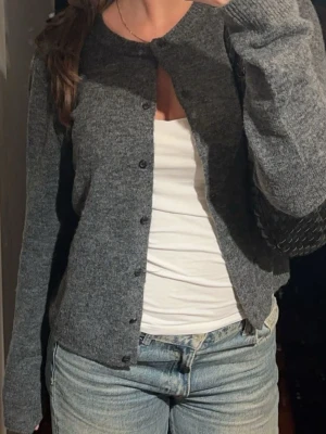 Mörkgrå kofta med knappar - Klassisk mörkgrå kofta med rund halsringning och svarta knappar framtill. Koftan har lång ärm och är gjord i ett mjukt stickat material. Storlek S från H&M🩶