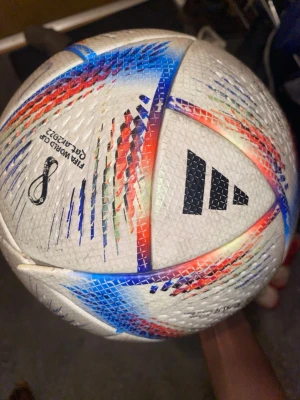 Adidas VM 2022 fotboll - Säljer en officiell FIFA World Cup Qatar 2022 fotboll från Adidas. Bollen är vit med färgglada detaljer i blått, rött och svart samt VM-logga tryckt på sidan. Klassisk rund form och tillverkad i slitstarkt syntetmaterial.
